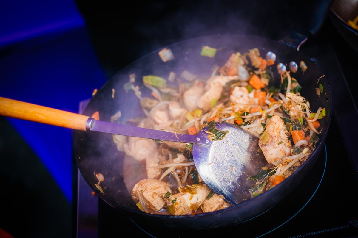 A wok with vegetables and ginger being stir-fried over a flame
